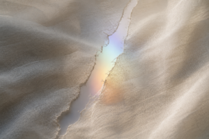 Torn ivory fabric revealing a soft rainbow light through the fracture